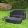 A black rattan sofa and coffee table set on a grassy lawn with a large rock and bushes in the background. Podgląd zdjęcia produktu