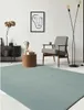 A modern living room with a light blue rug, a wooden side table with a bust and books, a patterned armchair, and a floor lamp. Produktbild-Vorschau