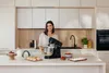 A woman is standing in a modern kitchen next to a black stand mixer. Náhled obrázku produktu