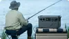 A person fishing by a lake with a portable power station next to them. Náhled obrázku produktu