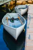 Two small boats docked next to a wooden pier, with rocks and water in the background. Produktbild-Vorschau