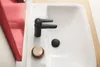 A close-up view of a modern black faucet in a white sink, with a wooden soap dish and a black drain cover. Anteprima dell’immagine prodotto