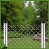 A chain-link fence with two metal posts in the foreground, with a blurred green background of trees and grass. Produktbild-Vorschau