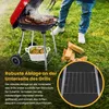 A person is grilling food on a charcoal grill in a grassy outdoor setting. There are logs of wood nearby. Produktbild-Vorschau