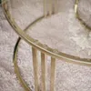 Close-up of a round glass coffee table with a gold metal frame, resting on a fluffy rug. Produktbild-Vorschau
