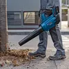 A person is using a leaf blower to clear leaves from the ground next to a tree. Produktbild-Vorschau