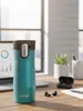 A teal Contigo travel mug sits on a wooden desk next to a laptop, earbuds, and a small potted plant. Produktbild-Vorschau