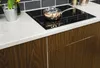 A close-up view of a kitchen countertop with a stovetop and a pot, next to wooden cabinets. Podgląd zdjęcia produktu