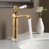 A vintage-style brass faucet with water flowing into a sink, next to a white vase with a flower. Náhled obrázku produktu