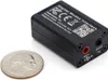 A small black electronic device with ports and text labels, placed next to a US quarter for scale. Produktbild-Vorschau