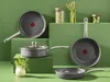 A collection of Tefal cookware arranged on green platforms with jars of green vegetables and asparagus in the background. Podgląd zdjęcia produktu