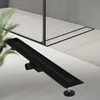 A black linear shower drain is shown on a tiled floor. Náhľad obrázku produktu