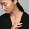 A woman wearing a black jacket and a silver necklace with a circular pendant. Anteprima dell’immagine prodotto