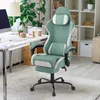 A gaming chair is shown in a home office setting next to a desk with a computer and plants. Produktbild-Vorschau
