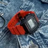 A digital watch with an orange strap rests on a denim jacket. Anteprima dell’immagine prodotto