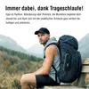 A man sitting on a bench in a mountainous landscape, wearing a backpack with a speaker attached. Produktbild-Vorschau