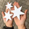 Hands holding white wooden stars on a paved surface. Produktbild-Vorschau