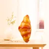 A croissant is placed on a table next to a vase with dried flowers, with a window and curtains in the background. Podgląd zdjęcia produktu