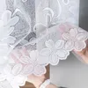 A close-up view of a white lace curtain with floral patterns, held by two hands. Náhled obrázku produktu