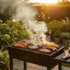 A barbecue grill with food cooking on it, set in a garden during sunset. Náhľad obrázku produktu