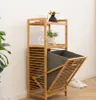 A bamboo laundry basket with a gray fabric liner is shown in a room with a plant and shoes. Náhľad obrázku produktu