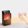A small electric heater with a realistic flame effect is shown on a shelf, with a person's hands being warmed by the heat. Anteprima dell’immagine prodotto