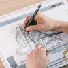 A person's hands are shown drawing an architectural design on a drafting board with a pencil and rulers. Náhľad obrázku produktu