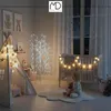 A child sits on a cloud-shaped rug in a nursery, holding a teddy bear, next to a crib decorated with string lights. A teepee with star lights is also visible. Podgląd zdjęcia produktu