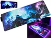 A collage of a large gaming mousepad with a nebula design and RGB lighting, shown both on its own and as part of a desk setup. Produktbild-Vorschau