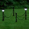 Two solar-powered garden lamps connected by a chain fence, set in a grassy garden with trees in the background. Produktbild-Vorschau