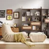 A cozy living room scene featuring a beige beanbag chair and ottoman, a wooden bookshelf filled with books and decor, and framed artwork on the wall. Náhled obrázku produktu