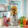 A retro-style blender filled with fruit, surrounded by fresh juices and ingredients on a kitchen counter. Produktbild-Vorschau