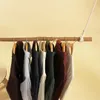 A collection of shirts and sweaters hanging on a rustic wooden rod. Produktbild-Vorschau
