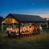 An outdoor evening dinner party under a tent with string lights. Produktbild-Vorschau