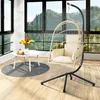 A hanging egg chair with cushions is placed on a wooden floor next to a small white table with a vase of flowers and some pastries. Large windows in the background reveal a scenic view of a forested mountain landscape. Voir les images du produit