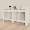 A white radiator cover with vertical slats is shown against a light wood-paneled wall and a light wood floor. Decorative items are placed on top of the cover. Anteprima dell’immagine prodotto