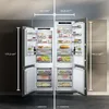 Two side-by-side refrigerator-freezer units with open doors, displaying their interior compartments and food items. Dimensions are indicated with measurement lines and text. Produktbild-Vorschau