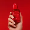 A hand holds a red perfume bottle against a red background. Podgląd zdjęcia produktu