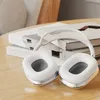 A pair of white and silver headphones are placed on a wooden table next to a stack of books. Podgląd zdjęcia produktu