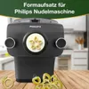 A Philips pasta maker attachment is shown on a wooden table with pasta shapes in the foreground and a blurred kitchen background. Podgląd zdjęcia produktu