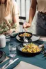 A table setting with food and cutlery, where someone is serving food from a bowl. Anteprima dell’immagine prodotto