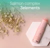 A pink balm stick is placed on a marble hexagon next to dried flowers, with a gradient background. Náhled obrázku produktu