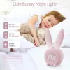 A child sleeping in bed with a stuffed animal, next to a pink bunny-shaped alarm clock. Produktbild-Vorschau