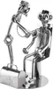 A metal sculpture of a doctor examining a patient, with a medical bag nearby. Anteprima dell’immagine prodotto