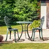 A metal bistro set with two chairs and a table is placed on a patio in a garden setting. Produktbild-Vorschau