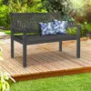 A dark gray wooden garden bench with two blue and white floral patterned cushions sits on a wooden deck surrounded by greenery. Náhled obrázku produktu