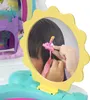 A close-up view of a child's hands styling pink hair with a small doll accessory, reflected in a sun-shaped mirror. In the background, a colorful toy castle with a rainbow arch is visible. Produktbild-Vorschau