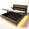 A modern upholstered bed frame with its storage compartment open, revealing wooden slats and the storage space below. The bed has integrated LED lighting around its base and headboard. Podgląd zdjęcia produktu