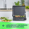 A countertop electric grill with food being cooked on it, placed in a kitchen setting with plates of food nearby. Produktbild-Vorschau