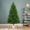 A green artificial Christmas tree stands on a rug with gifts underneath, in a room with a shelf and star decoration. Produktbild-Vorschau